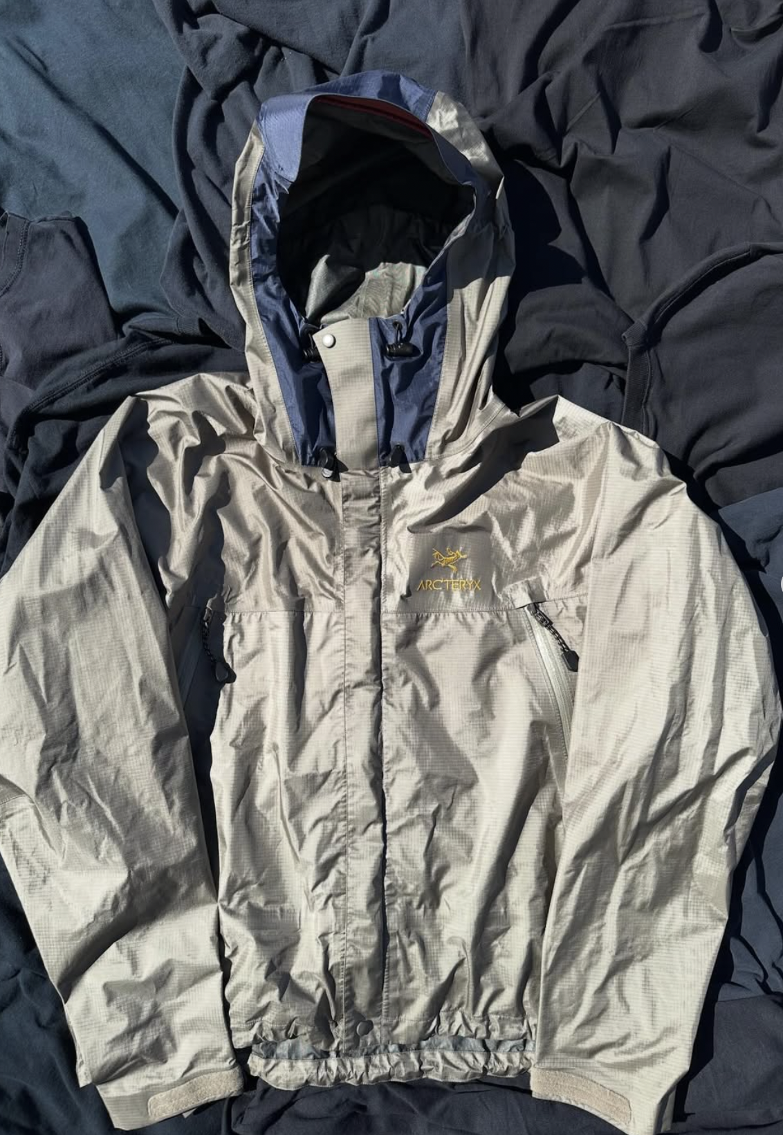 Vintage tan lightweight windbreaker with hood, laid flat on navy fabric.